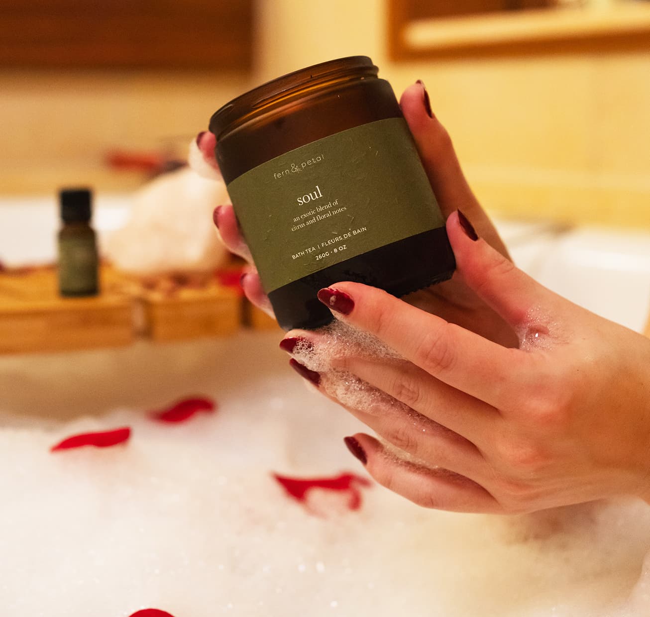 A container of soul being held above a rose petal filled bath tub